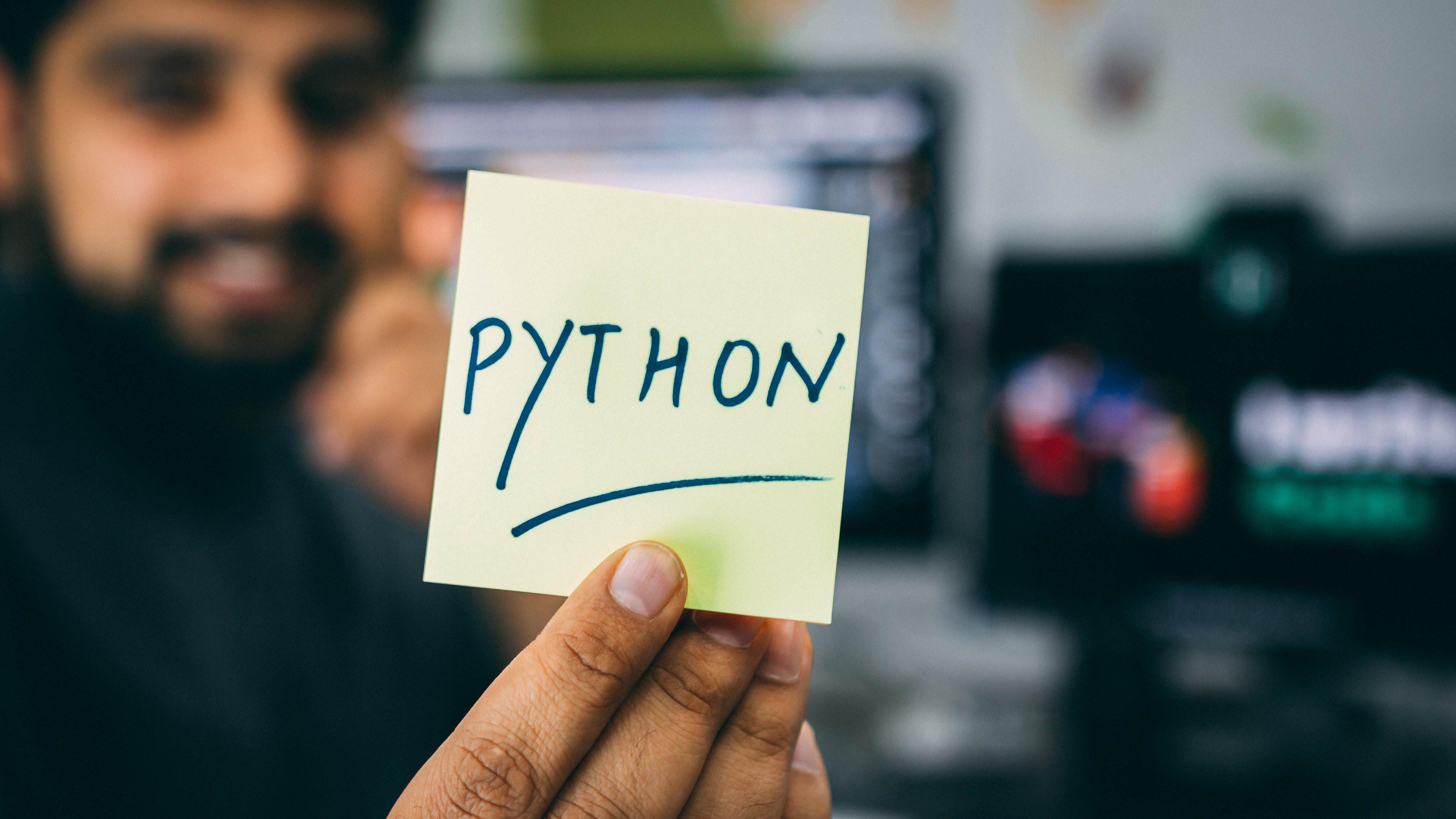 Man holding a post it note with Python written on it (macro shot with blur background)